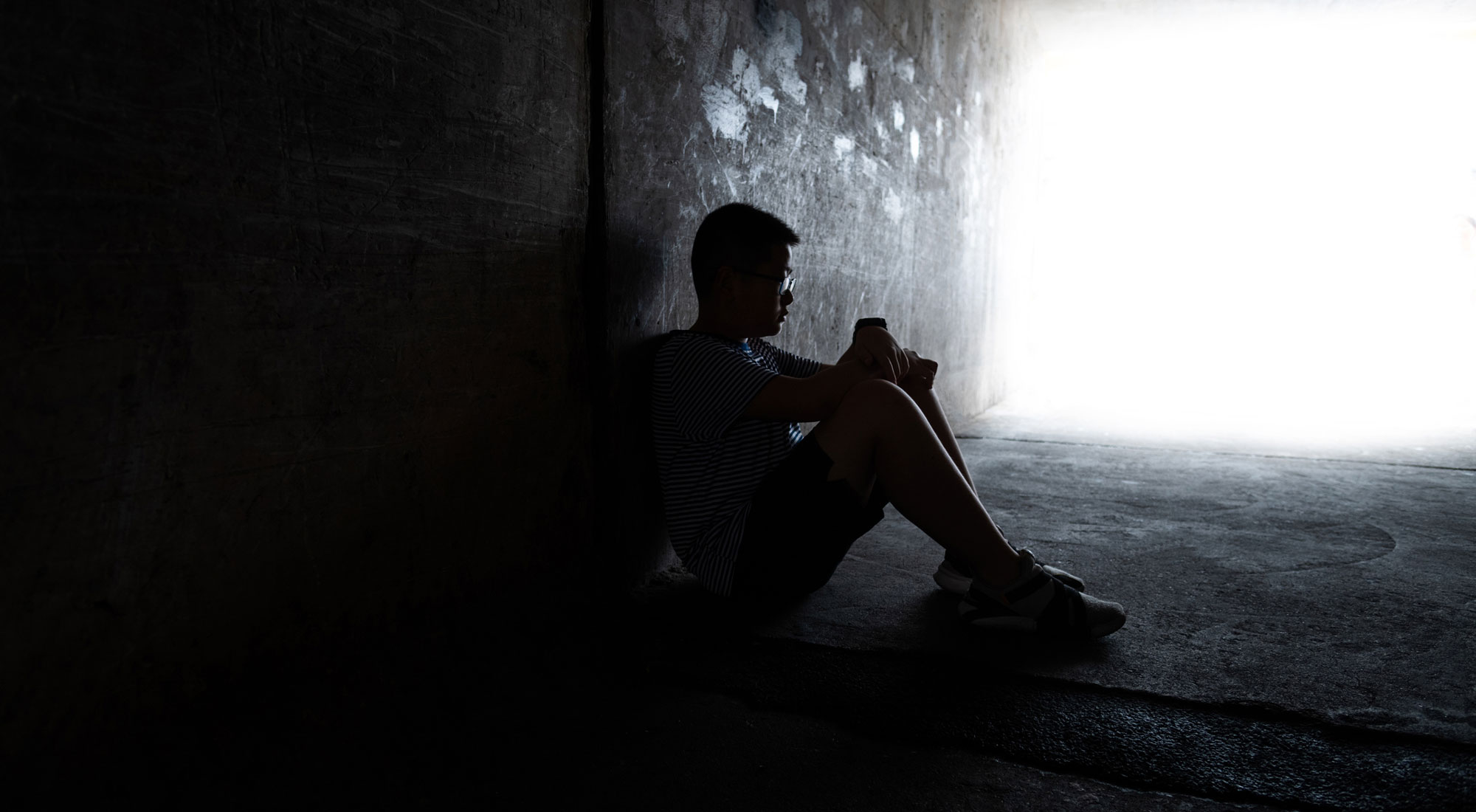 teenage boy sitting alone in dark tunnel