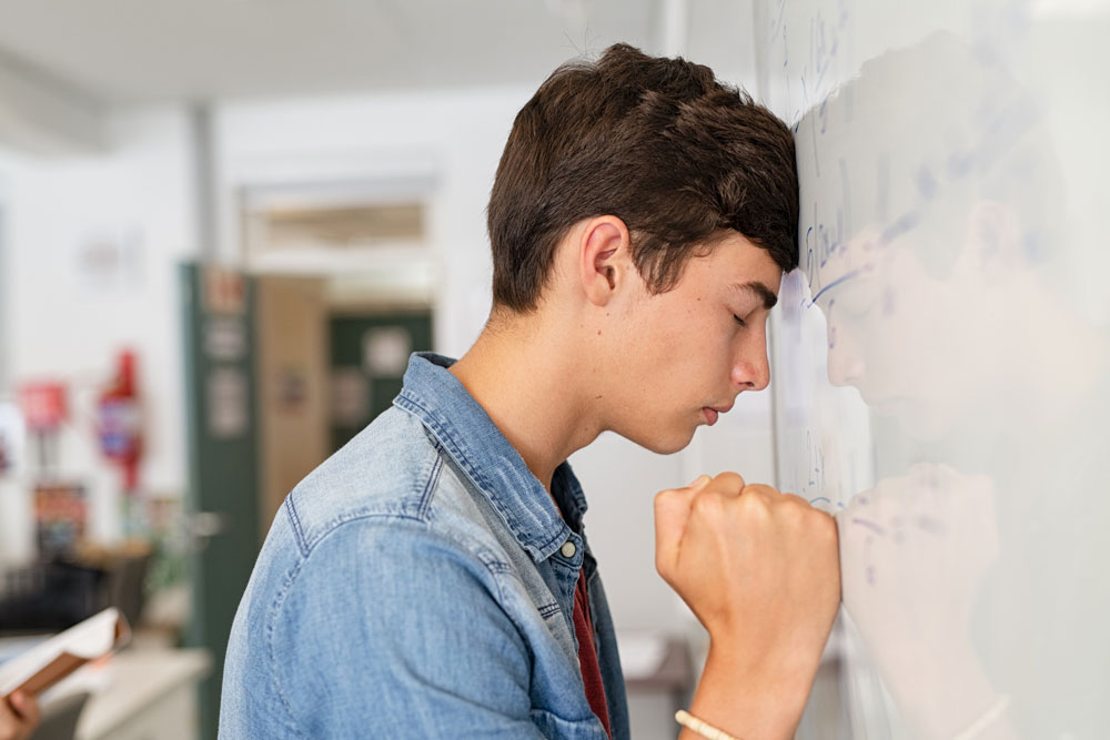 teenage boy with head on white board experiencing anxiety